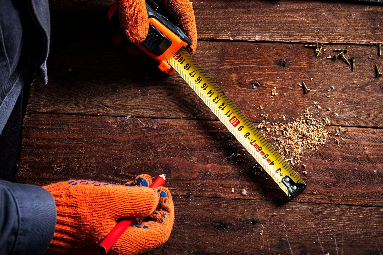 Gloved hands measuring a wood board during layout
